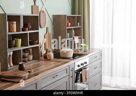 Modernes Kücheninterieur mit Holzarbeitsplatten, grauen Schränken, offenen Regalen und Kochutensilien Stockfoto
