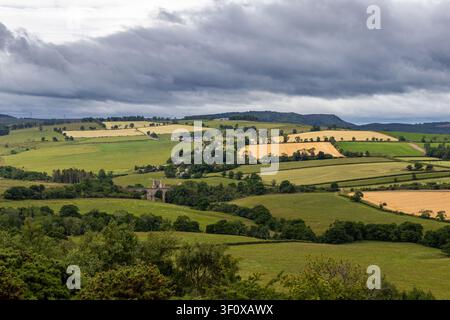 Ruinen von Edlingham Castle neben Steinviadukt inmitten Flickenteppich-Feldern unter Sturmwolken Stockfoto