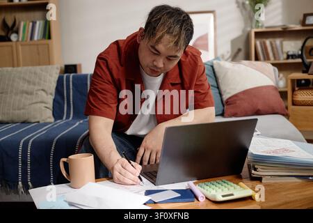 Asiatischer Mann, der den Haushaltsbudget verwaltet und Rechnungen zu Hause bezahlt Stockfoto