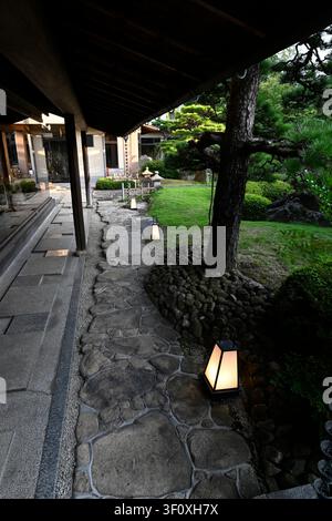 Ein traditioneller Steinpfad, der von Laternen beleuchtet wird, windet sich durch die Gärten des Hanbe Garden, dem historischen Kaiseki-Restaurant in Hiroshima, Japan. Co Stockfoto