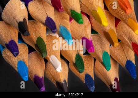 Leuchtend farbige Bleistifte mit gespitzten Spitzen sind eng aneinander gedrängt vor einem dunklen Hintergrund und zeigen eine lebendige Farb- und Texturvielfalt Stockfoto