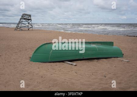 Grünes Fischerboot am Strand und ein schiefer Beobachtungsturm im Hintergrund Stockfoto