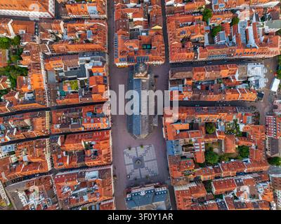 Luftaufnahme der historischen Heiliggeistkirche, die sich im belebten Marktplatz befindet, umgeben von dichten rotgedeckten Dächern und traditioneller Architektur Stockfoto