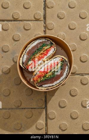 Sushi-Burger auf gelben texturierten Pflastersteinen. Lieferbox. Isoliert. Kunstvolles Foto. Professionelles Studiolicht. Stockfoto