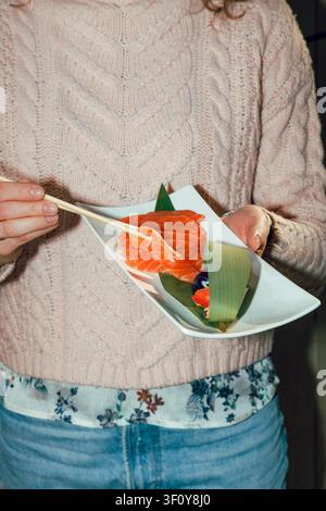 Mädchen isst Lachs-Sashimi mit Stäbchen von einem weißen Teller Stockfoto