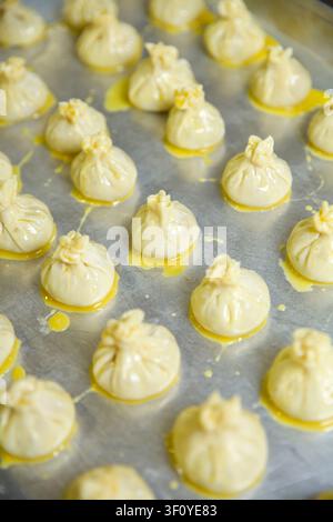 Knödel sind ordentlich auf einem Metalltablett mit einer Schicht Öl angeordnet. Die Kücheneinrichtung zeigt die Vorbereitungsphase, bevor das Kochen beginnt. Stockfoto
