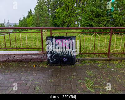 Mülltonne mit Graffiti auf nassem Bürgersteig der Stadt. Stockfoto