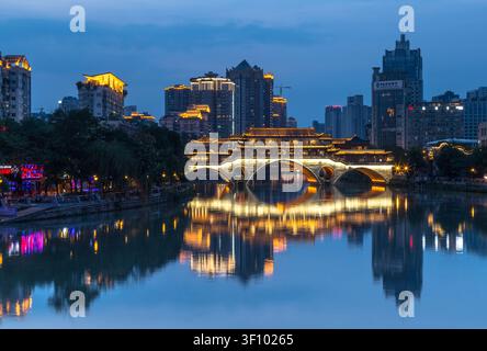 Wunderschöner Nachtblick auf die beleuchtete Anshun-Brücke und moderne Wolkenkratzer, die sich im Jin-Fluss in Chengdu, Sichuan, China spiegeln. Stockfoto