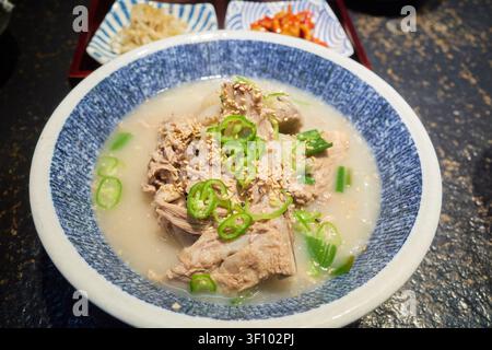 Traditionelle Jeju-Insel-Schwein-Knochensuppe und Buchweizensuppe, garniert mit grünen Chilischoten und Sesamsamen in einer blau gemusterten Schale, die authentische Regi präsentiert Stockfoto