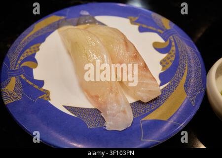 Verschiedene Premium-Nigiri-Sushi-Sorten, darunter frischer Weißfisch und gebratener Fisch mit Kreuzhatch-Schnitt, serviert auf bunten Tellern an einem modernen Transportband Stockfoto
