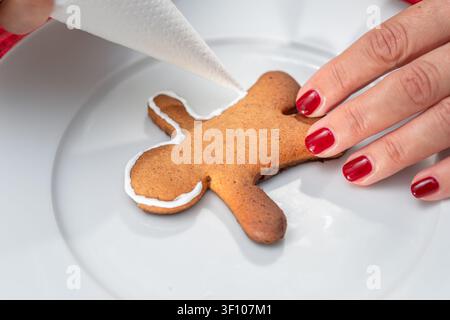 Weihnachtskekse machen - Lebkuchenmänner, eine Frau dekoriert Kekse mit königlicher Glasur. Stockfoto