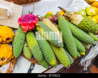 Grüne exotische Bananen-Ananasfrüchte von Monstera deliciosa, ausgestellt in einem Korb an einem traditionellen Obststand auf Madeira, Portugal. Stockfoto