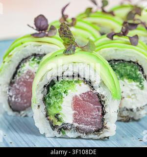 Sushi-Rollen mit grünen und weißen Belägen, die auf einem blauen Teller arrangiert sind. Stockfoto