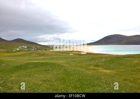 Landschaftsansicht einer sandigen Bucht, türkisfarbenem Meer, grasbewachsenen Küstenhügeln und entfernten Häusern in den Äußeren Hebriden, Schottland Stockfoto