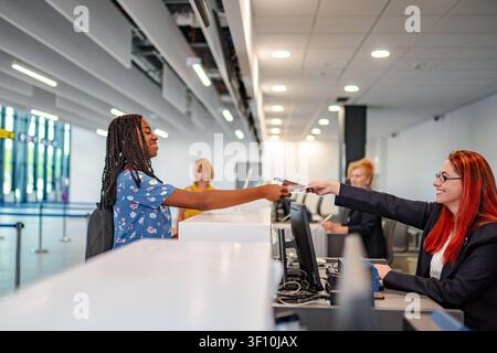 Junge Frau checkt am Flughafen mit einem Reiseberater ein Stockfoto
