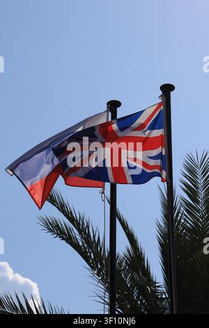 Fahnen wehen an Flaggenmasten und die britische Flagge verdeckt die russische im Gegenlicht in vertikaler Ausrichtung Stockfoto