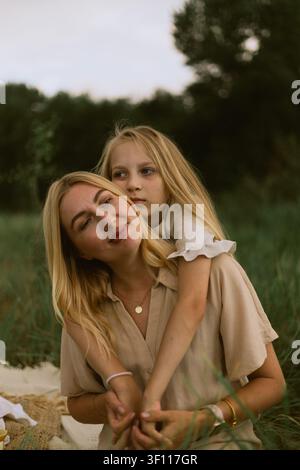 Eine liebevolle Mutter und ihre Tochter teilen einen zarten Moment im Freien, umgeben von üppigem grünem Gras und Bäumen Stockfoto