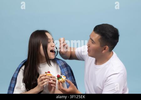 Junger Mann füttert seine Freundin mit einem köstlichen Fast-Food-Snack Stockfoto