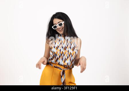 Fröhliche junge Frau mit Sonnenbrille, die posiert und in guter Stimmung tanzt Stockfoto