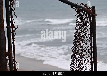 Verrosteter Maschendrahtzaun mit Blick auf die Pazifikküste und Wellen im Hintergrund. Stockfoto
