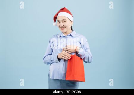 Lächelnde junge Frau mit einem Weihnachtsmannhut, die eine rote Weihnachtstüte hält Stockfoto