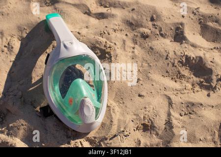 Schnorchelmaske, die auf sandigem Strand ruht, Sonnenlicht beleuchtet die klare Linse und die lebendigen Farben der Ausrüstung Stockfoto