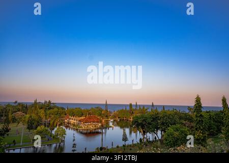 Panoramazug mit tropischen Gärten, Küstenvegetation und ruhigem Ozean, der sich unter einem farbenfrohen Dämmerungshimmel erstreckt. Stockfoto