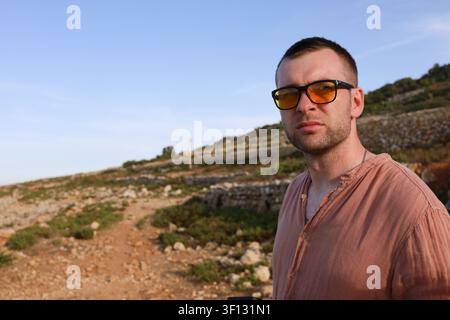 Valletta, Malta, 19. Juni 2026. Porträt eines männlichen Touristen mit Sonnenbrille auf einem hügeligen Küstenpfad. Stockfoto