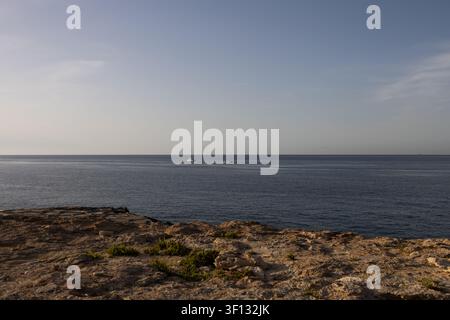 Prachtvolle Aussicht auf ein ruhiges blaues Meer mit fernen Booten von einer felsigen Kalksteinküste in Malta. Stockfoto