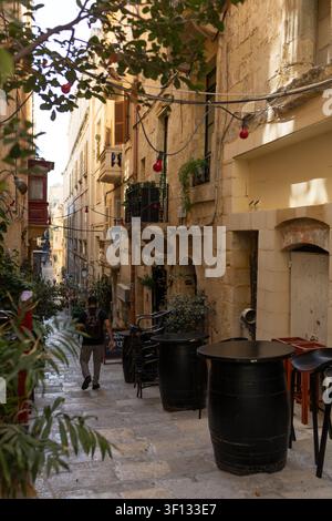 Leere Außenterrasse einer Bar mit Holzkesseltischen auf einer schmalen historischen Straße in Valletta, Malta. Stockfoto