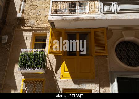 Traditionelle gelbe Holzläden und Balkone an einer historischen Steinfassade in Malta. Stockfoto