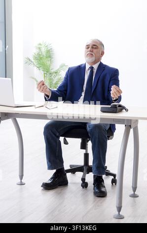 Alter Geschäftsmann Yoga Übungen im Büro Stockfoto