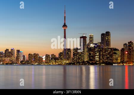 TORONTO, KANADA — 17. SEPTEMBER 2017: Vertikale Aufnahme des CN-Turms, der in der Dämmerung beleuchtet ist, mit der Skyline der Innenstadt über dem Ontariosee. Stockfoto