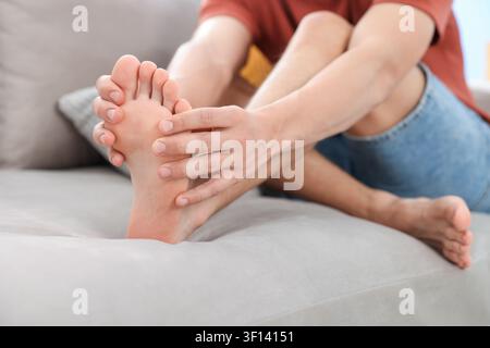Mann massiert seinen Fuß auf dem Sofa zu Hause, Nahaufnahme Stockfoto