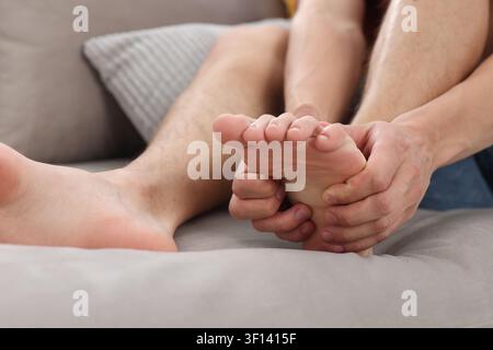 Mann massiert seinen Fuß auf dem Sofa zu Hause, Nahaufnahme Stockfoto