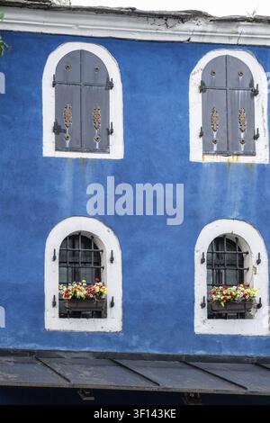 Blaue Fassade eines alten Hauses teilweise mit Blumen am Fenster und im Obergeschoss mit geschlossenen Fensterläden Stockfoto