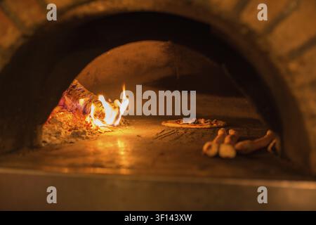 Eine Pizza und ein Pizzabrot werden in einem mit glühendem und brennendem Holz befeuerten Pizzaofen gebacken Stockfoto