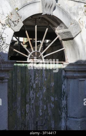 Verwitterte, gewölbte Steintür mit einem verfallenden grünen Holztor und einem verzierten, verrosteten Metallgitter. Ein Blick in die Vergangenheit Stockfoto