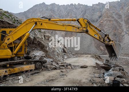 Ein großer gelber Kettenbagger arbeitet daran, Felsbrocken und Schutt von einer Schotterbergstraße in Ladakh, Indien, zu entfernen und einen von einer Lanze versperrten Weg freizuräumen Stockfoto