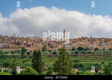 Ein Stadtpanorama zeigt die historische Medina von Meknes, die sich über den Horizont erstreckt, einen hohen Minarett, der über den ockerfarbenen Dächern aufragt, und das grüne V Stockfoto