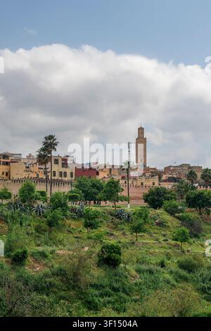 Eine Panoramaaussicht von den Höhen über Meknes zeigt die Dächer der Medina und einen hohen Minarett, der über dem städtischen Gefüge aufragt, grüne Bäume und Gärten bel Stockfoto