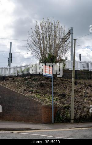 Eine vertikale Ansicht des Schildes des Pangbourne-Bahnhofs, das das klassische britische Rail-Doppelpfeil-Logo zeigt, das unter einem Baum an der Bahnstrecke platziert ist Stockfoto
