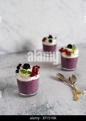 Gesunder geschichteter Beeren-Chia-Pudding, serviert in Gläsern und mit Schlagsahne und frischem Obst belegt Stockfoto