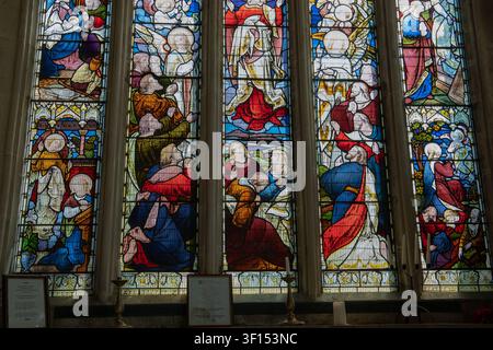 Detailliertes Buntglasfenster in einem Kircheninneren, das farbenfrohe religiöse Figuren und biblische Szenen darstellt, mit Licht, das durch das Glas scheint Stockfoto