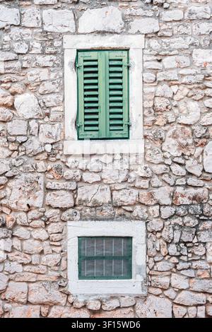 Steinerne Wand mit grünen Holzläden an einer alten rustikalen Gebäudefassade. Stockfoto