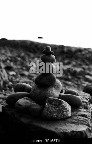Schwarz-Weiß-Nahaufnahme eines ausgewogenen Stapels glatter Steine, die einen Zen-Kreis auf einer felsigen Oberfläche bilden und Balance und Ruhe symbolisieren Stockfoto