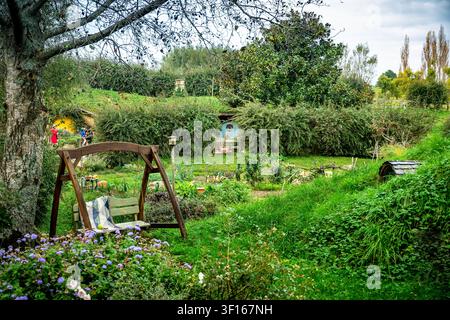 Eine friedliche Gartenlandschaft am Filmset von Hobbiton in Matamata, Neuseeland, mit einer hölzernen Gartenschaukelbank, die sich zwischen üppigen grünen Rasenflächen befindet Stockfoto