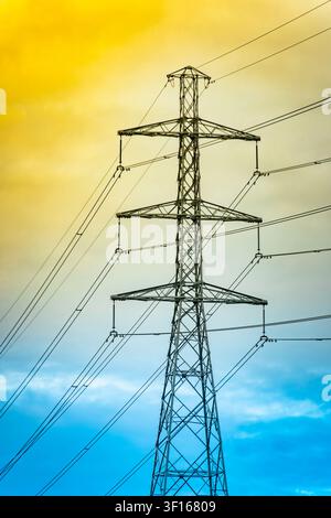 Ein Strommast ragt hoch gegen einen dramatischen Gradientenhimmel, der sich von warmem Gelb zu tiefem Blau verzieht. Stockfoto