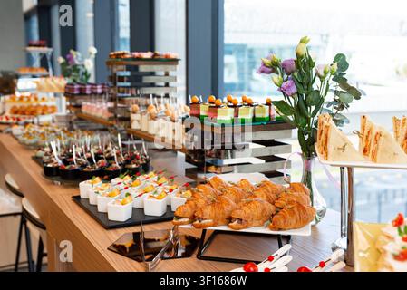 Verschiedene Snacks und Desserts, ordentlich auf einem modernen Buffettisch mit Blumen in der Veranstaltungsstätte arrangiert. Stockfoto