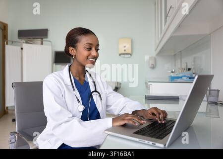 Zufriedene junge afrikanische Allgemeinärztin arbeitet am Computer Stockfoto